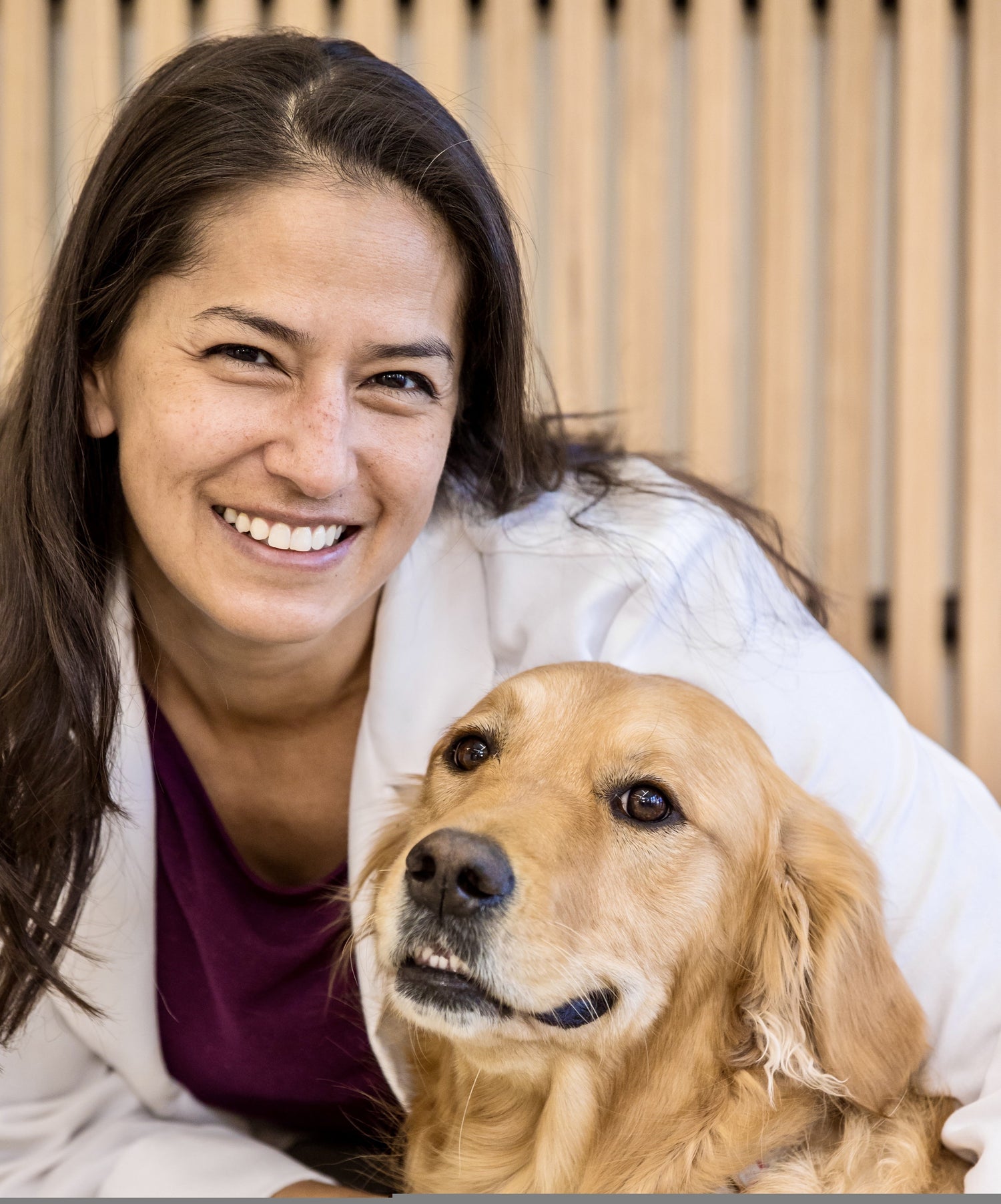 Woman in a white coat with a golden retriever dog indoors.
